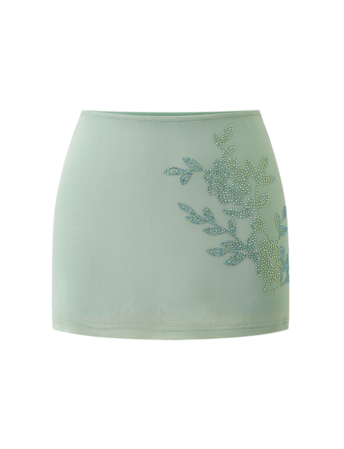 The OCTAVIA MINI SKIRT in pistachio by TIGERMIST features a light green hue and rhinestone floral embellishment on one side, showcased against a plain white background.