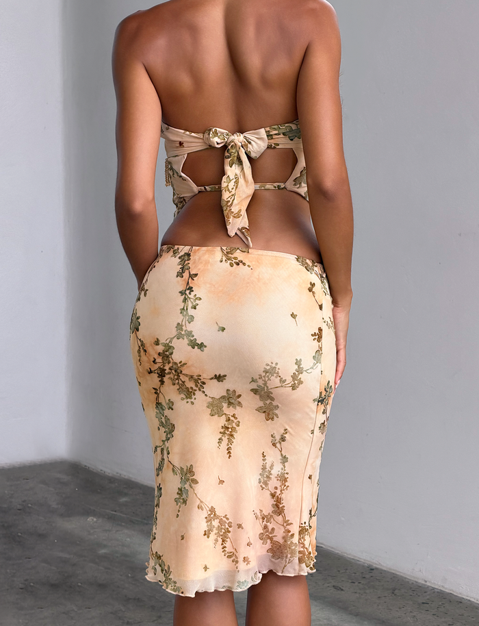 A person stands indoors with their back to the camera, wearing the TIGERMIST OONA BURN OUT FRINGE TOP in tan. The setting has a concrete floor and a plain light gray wall in the background.