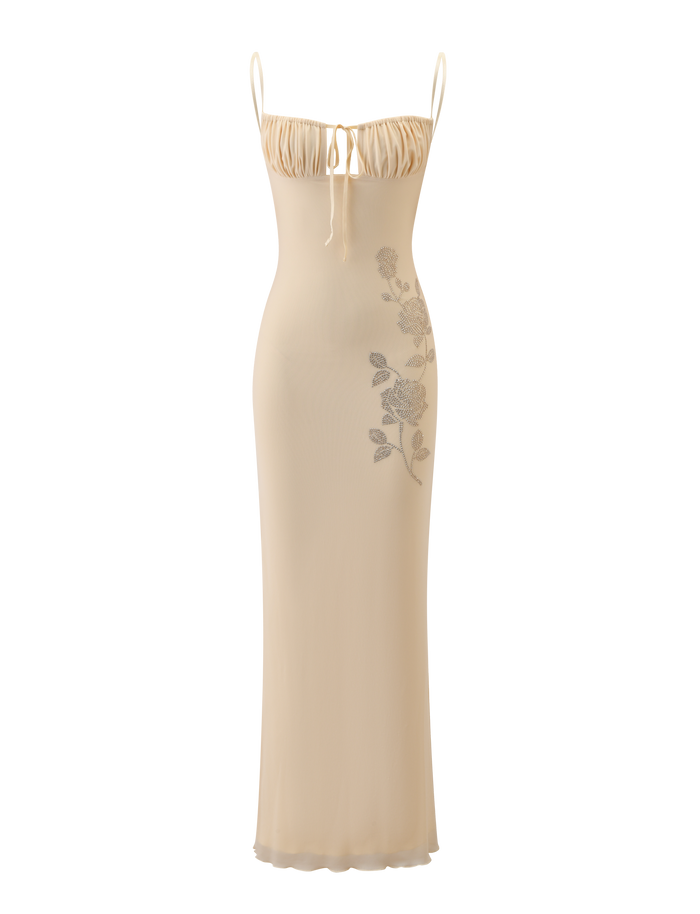 The OPHELIA MAXI DRESS by TIGERMIST features a cream hue, adjustable spaghetti straps, a gathered bust with a dainty bow, and delicate floral detailing along one side.