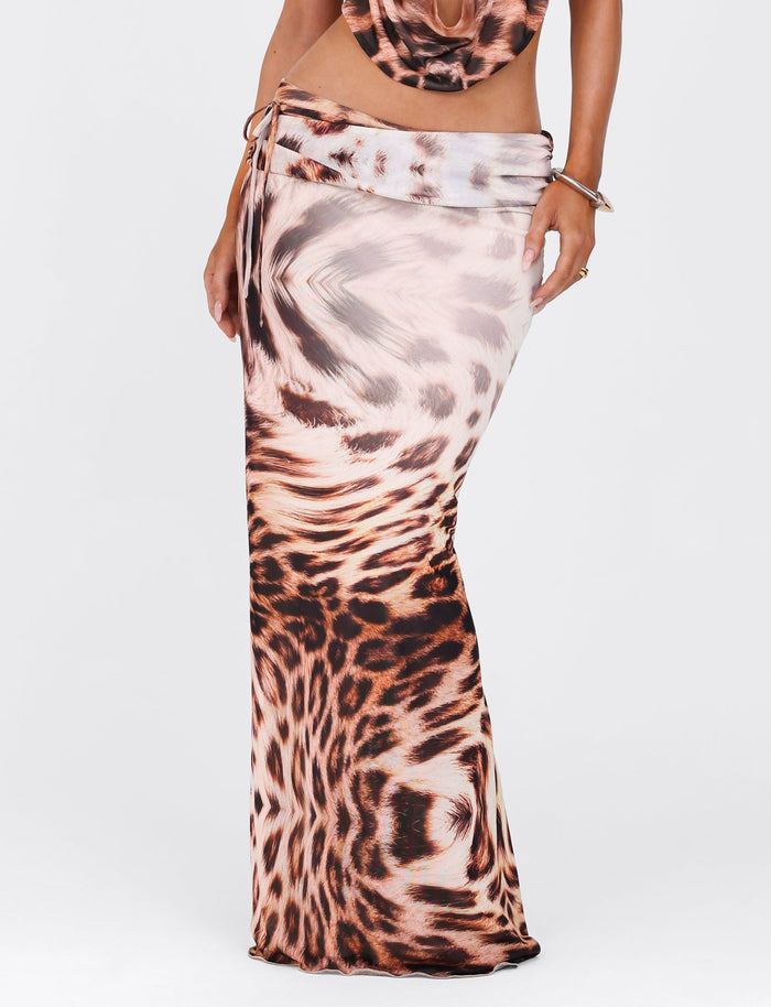 A person dressed in the TIGERMIST Pearl Maxi Skirt - Neutral Leopard Haze. This long, form-fitting skirt showcases a relaxed silhouette featuring a wrap-around design and tie at the waist, set against a plain light background.