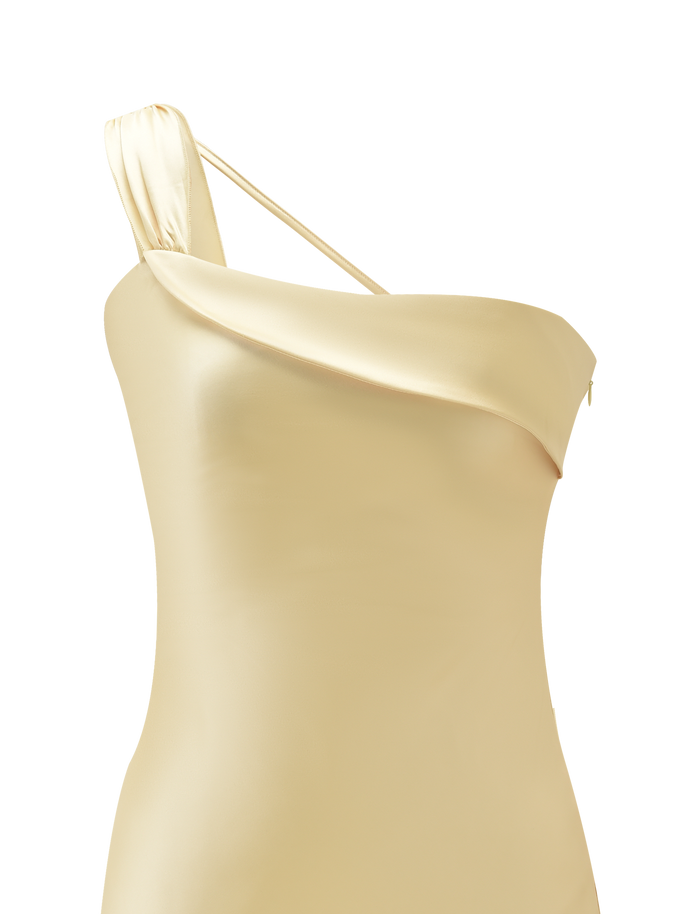 A close-up of the TIGERMIST RAINEY MINI DRESS in Butter, a one-shoulder satin dress with a draped neckline, asymmetric strap, and subtle waterfall ruffle detail, displayed on a plain white background.