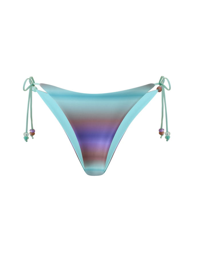 The REVERSIBLE FINLEA BIKINI BOTTOM - MERMAID OMBRE STRIPE by TIGERMIST features a cheeky bikini cut with gradient blue, purple, and teal shades accented by beaded side ties, shown on a plain white background.