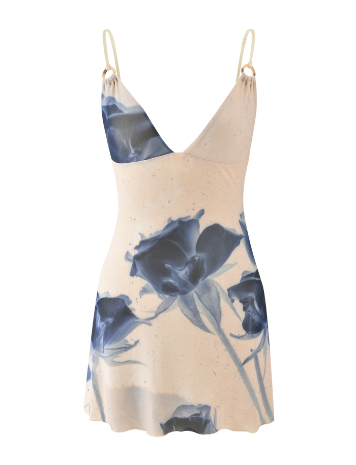 The TIGERMIST ROSY MINI DRESS - INDIGO FLORAL is a sleeveless cream mini dress with adjustable cami straps, a wrap-style neckline, and a bold blue rose print on the front.