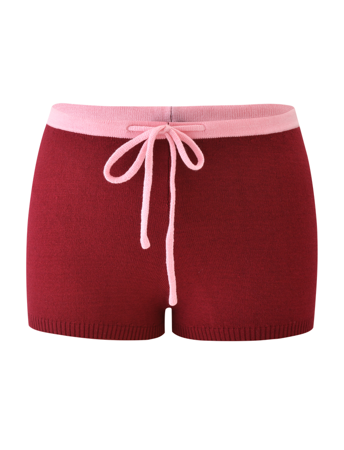 The ROUX SHORT - RED by TIGERMIST features a red knit design with a wide pink waistband, pink front drawstring bow, and an asymmetrical star graphic for a stylish touch.