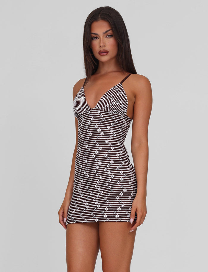 A woman with long dark hair wears the TIGERMIST SAHRA MINI DRESS in chocolate brown stripe, a fitted, sleeveless style with thin straps, standing against a plain light gray background.