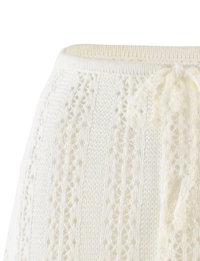 Close-up of the SANDOR SKIRT - WHITE from TIGERMIST showcasing its intricately knit design with small holes and a decorative yarn bow at the waistband. The texture appears soft and detailed, featuring a ribbed edge at the top.