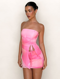 A woman stands against a plain light background, wearing the TIGERMIST SARIAH TOP in Macro Floral Pink Blossom with a strapless, bodycon fit and ruching. Her hair is in a sleek bun as she looks slightly to the side.