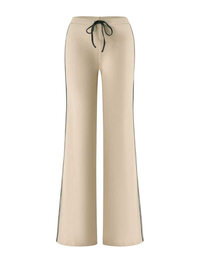 The SHANICE LOUNGE PANT - SAND by TIGERMIST features a beige flared silhouette with a black drawstring waist and contrasting black side stripes, crafted from stretch jersey fabric for enhanced comfort, shown against a white background.