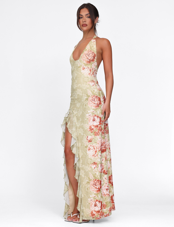 A woman poses against a white background wearing the TIGERMIST SIRENA MAXI DRESS in yellow floral rose stripe, featuring a halter neck, ruffled details, and a high split. Her hair is tied back.