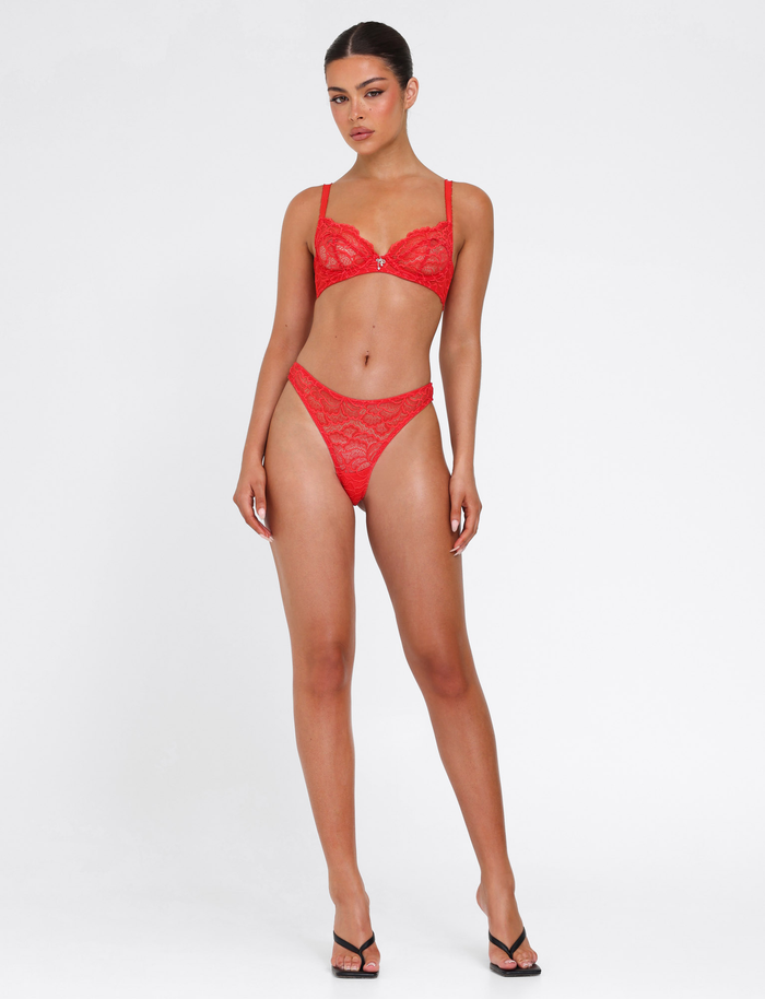 A woman stands against a white background wearing the SIRENE SET 2.0 - RED by TIGERMIST, a red lace matching intimate set with high-waisted panties and black heels. She faces forward with a neutral expression, arms at her sides.
