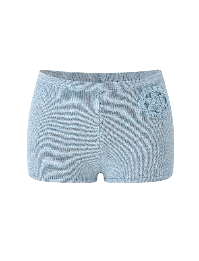 The TIGERMIST SUNIA SHORT - BLUE features ultra-mini, light blue hot shorts with a high waist and a subtle crocheted flower appliqué on the left hip, showcased against a plain white background.