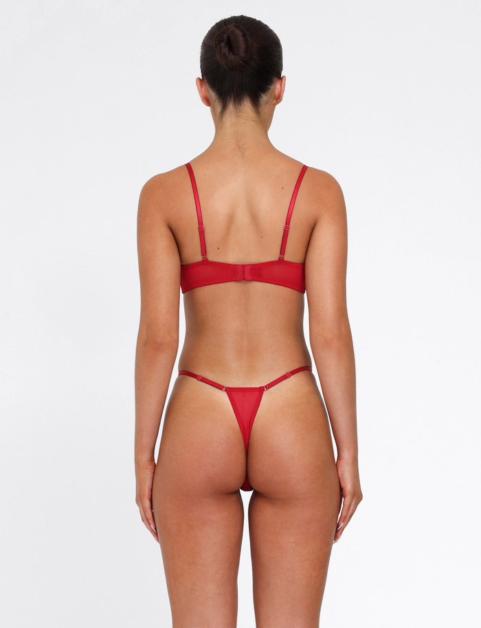 A woman with her hair in a neat bun faces away from the camera, wearing the TIGERMIST TALIYAH SET - RED, a matching 2-piece bra and thong set, against a plain white background.