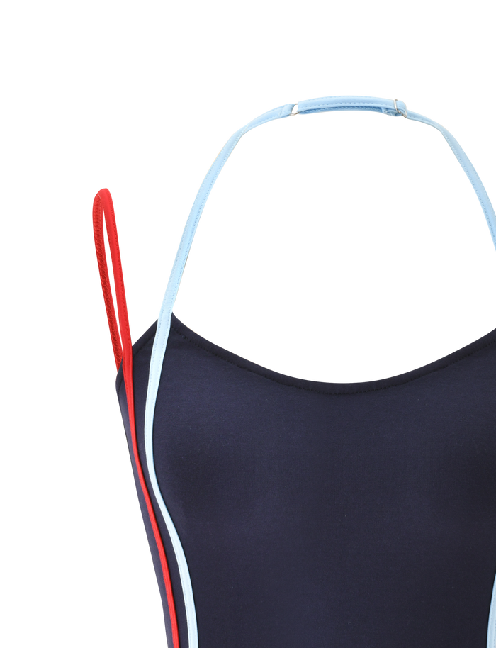 A close-up of the TIGERMIST TATUM TOP - NAVY STRIPE, featuring an open back, one red and one light blue shoulder strap, and light blue piping, displayed on a plain white background.