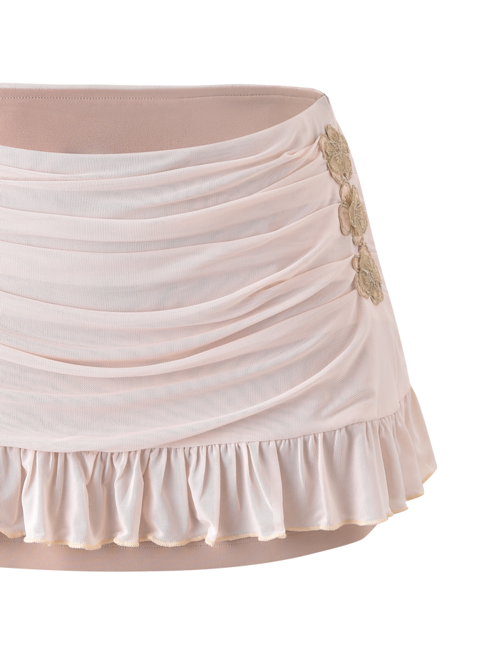 The TERESE FLORAL APPLIQUE SKIRT in tan by TIGERMIST features ruching, a ruffled hem, and three gold floral appliqués on one side, shown against a plain white background.