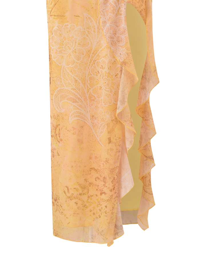 A close-up of the TIGERMIST THEO SKIRT - LEMON BUTTERFLY PAISLEY, a yellow low-rise maxi with white paisley patterns, soft ruffled edges, and a front leg slit revealing a light beige inner layer.