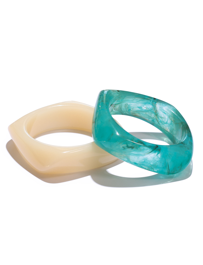 The TIGERMIST TIA CHUNKY 2PC RESIN BANGLE SET features bold, geometric bangles in cream and marble-like blue resin, stylishly stacked together against a white background.