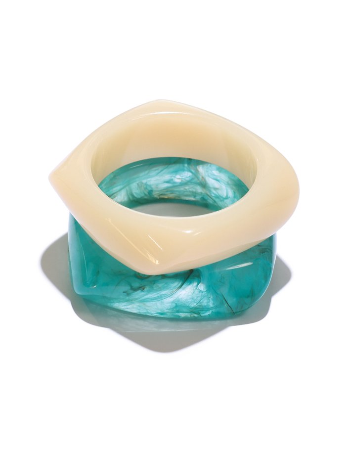 The TIGERMIST TIA CHUNKY 2PC RESIN BANGLE SET features a cream geometric resin bangle stacked above a translucent blue, marble-finished square bangle for a bold layered look.