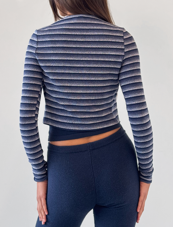 A person with long brown hair is seen from behind wearing the TIGERMIST TIMARA CARDIGAN in navy stripe and dark blue fitted pants, set against a plain, light-colored background.