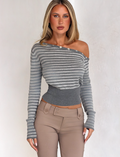 A woman with long blonde hair wears the TIGERMIST TYLA JUMPER in grey stripe, featuring an off-the-shoulder neckline and collar buttons, paired with beige high-waisted pants against a neutral background.