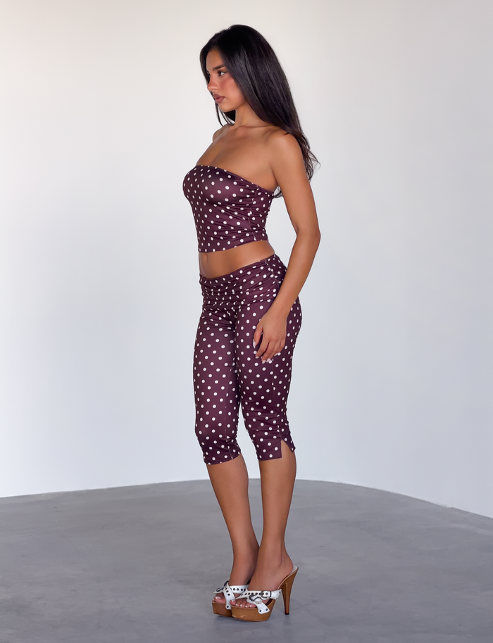A woman stands in profile against a plain background, wearing the TIGERMIST VALI POLKA DOT TOP in chocolate pink dot, paired with capri pants and high-heeled platform sandals for a chic, coordinated look.