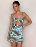 A woman poses against a plain background, wearing the TIGERMIST VERA MINI DRESS in MULTI: ANIMAL: BUTTERFLY ANIMAL with cut-out details, thin straps, and a colorful butterfly print. Her hair is slicked back and her expression neutral.