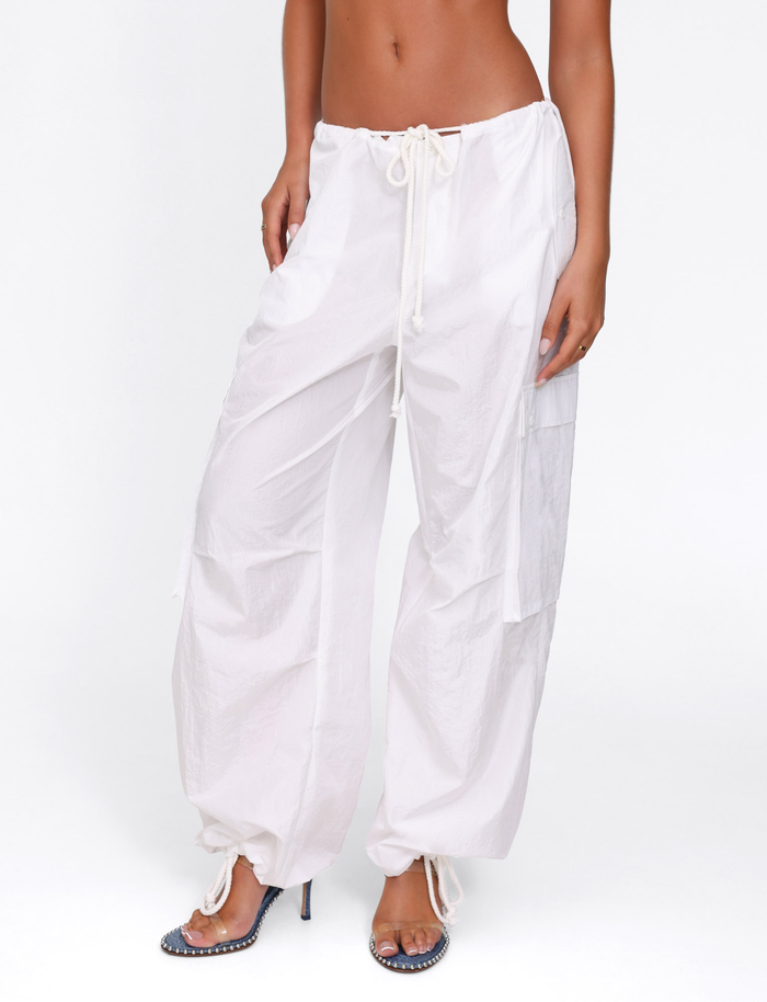 A model wears the TIGERMIST VIOLETTE PANT in white—an oversized fit with drawstring waist and gathered cuffs—paired with high-heeled sandals, shown from mid-torso to feet against a plain white background.
