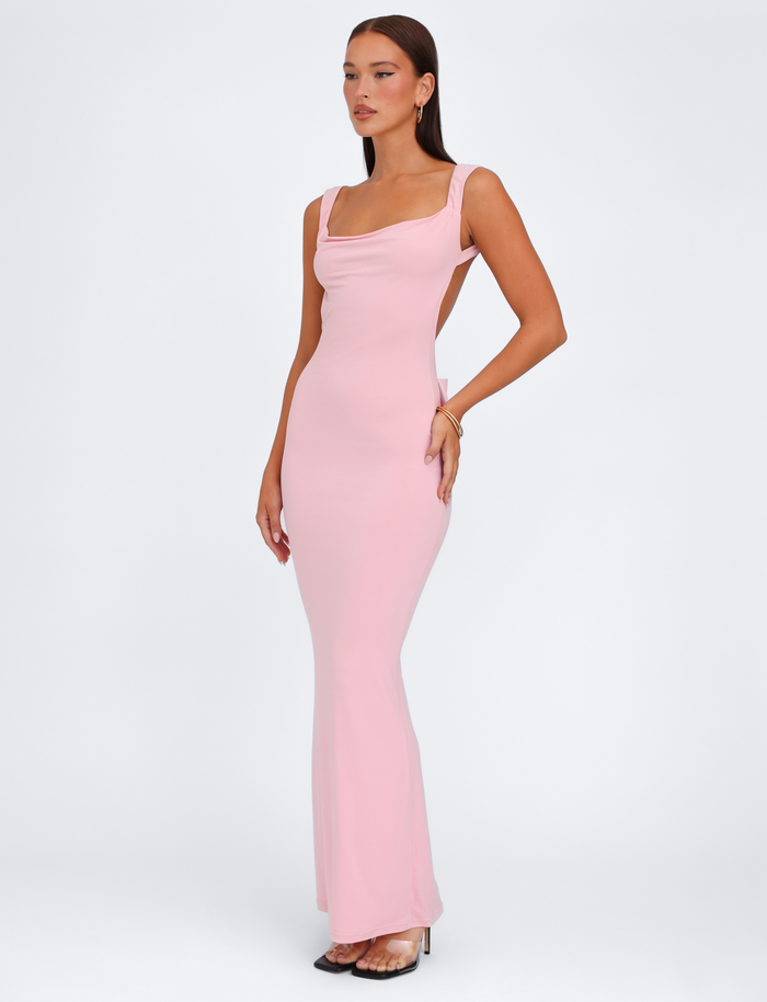 A woman models the TIGERMIST ZITA DRESS - PINK : BABY PINK, showcasing its bodycon fit and square neckline. She pairs it with clear heels and gold jewelry, standing against a plain white background.