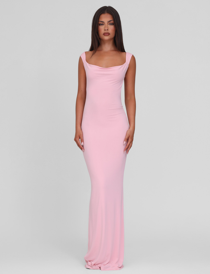 A woman faces forward, wearing the TIGERMIST ZITA DRESS in baby pink—a fitted, sleeveless bodycon maxi dress with a draped neckline—against a plain light gray background.