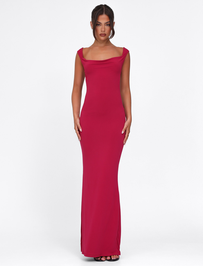 A woman stands against a white background wearing the TIGERMIST ZITA Dress - Red : Salsa : Deep Red, a sleeveless bodycon maxi dress with a slight cowl neckline, styled with black open-toe heels and her dark hair in a center-parted updo.