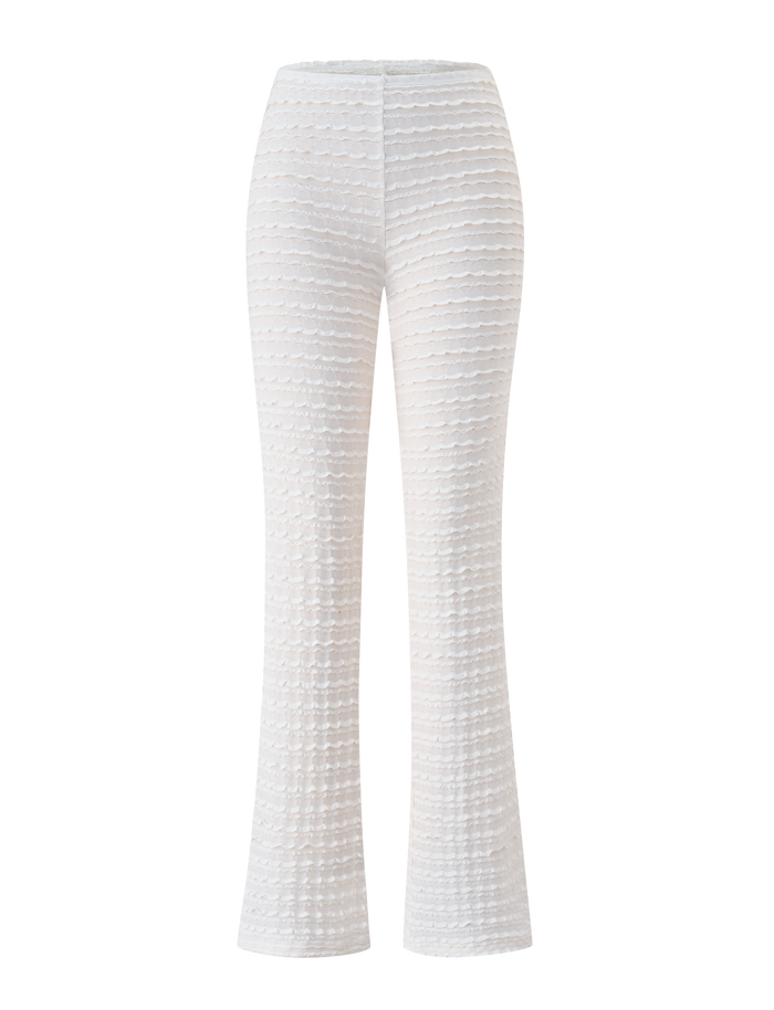 The TIGERMIST ZORA PANT in cream features a wavy, layered texture, high waist, flared leg, and subtle ruffle detail. Ideal as a beach cover-up, these pants are shown on a plain white background.