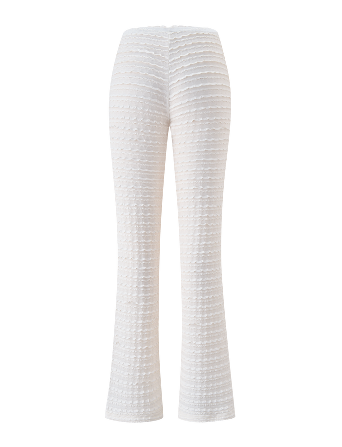 The ZORA PANT - CREAM by TIGERMIST features a high waist, textured flared fit, layered horizontal pattern, and subtle ruffle detail—shown from the back against a white background. Ideal as a trendy beach cover up.