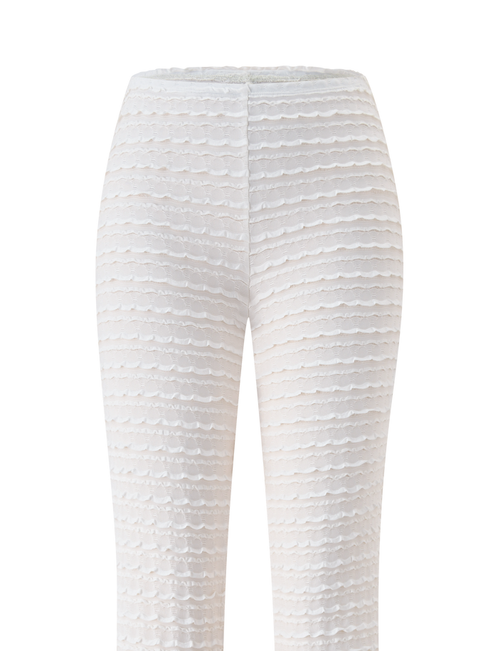 The ZORA PANT - CREAM by TIGERMIST features a white textured, high-waist design with a subtle wavy pattern and ruffle accents. This form-fitting style is ideal as a chic beach cover up, shown against a plain white background.